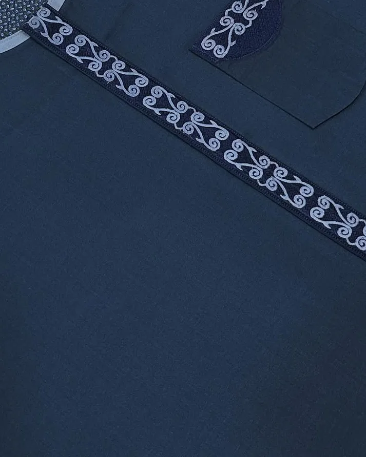 Detail of white scroll embroidery on a navy garment panel in the atelier